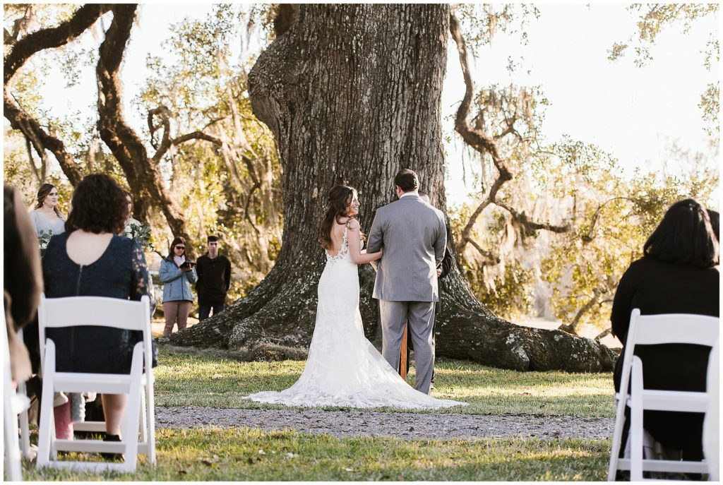 couple stands in front of oak tree for wedding ceremony in Louisiana