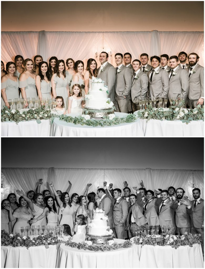 large bridal party poses with cake at wedding reception