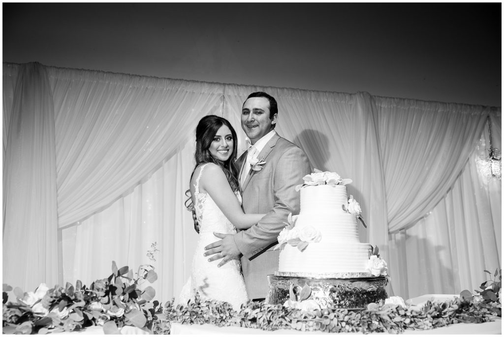 bride and groom pose with wedding cake at reception