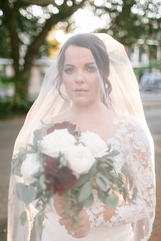 bride wears blusher veil and holds burgundy and white bouquet