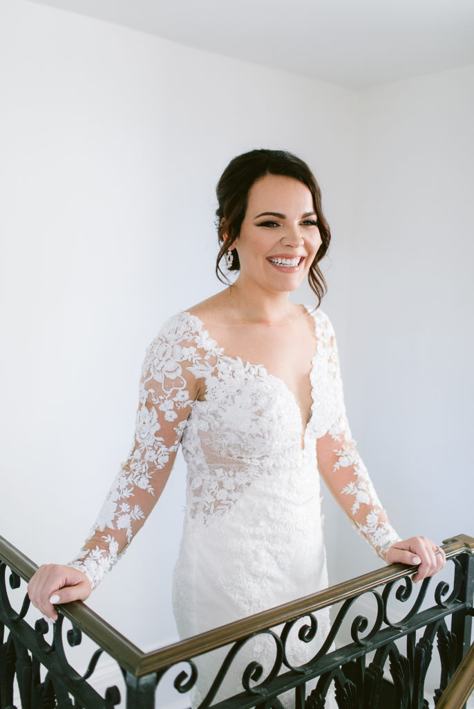 bride stands with wrought iron bannister in wedding gown