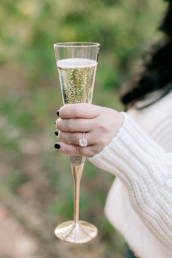 woman holds champagne glass to show engagement ring